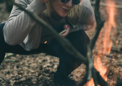 woman in sunglasses with phone crouching by campfire