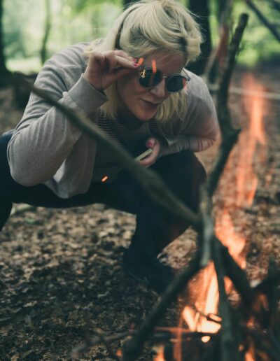 woman in sunglasses with phone crouching by campfire