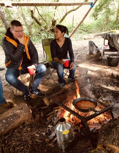 two adults cooking beans on campfire