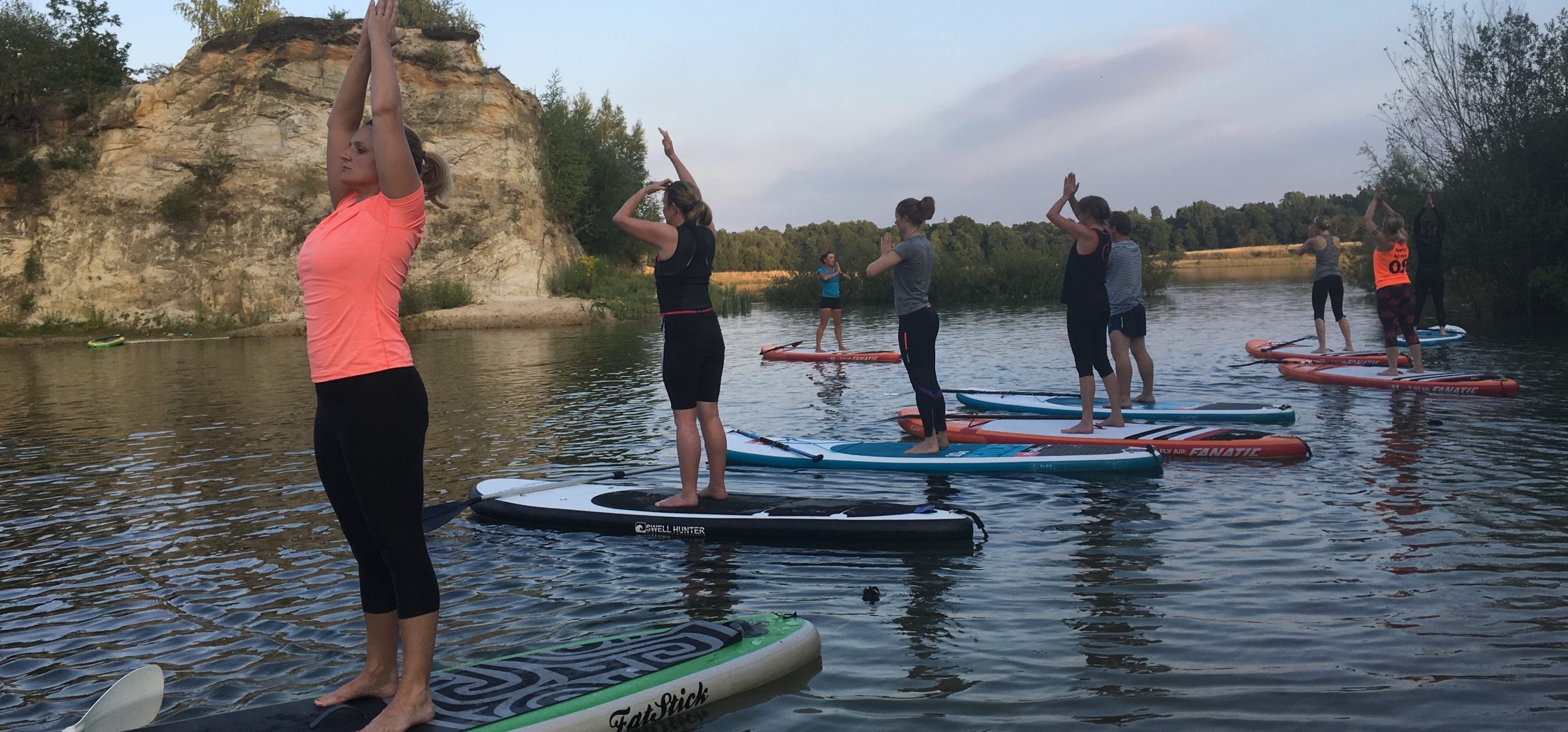 SHAC Buckland yoga group standing with arms above head on paddleboards SHAC Buckland SUP yoga group standing with arms above head on paddleboards