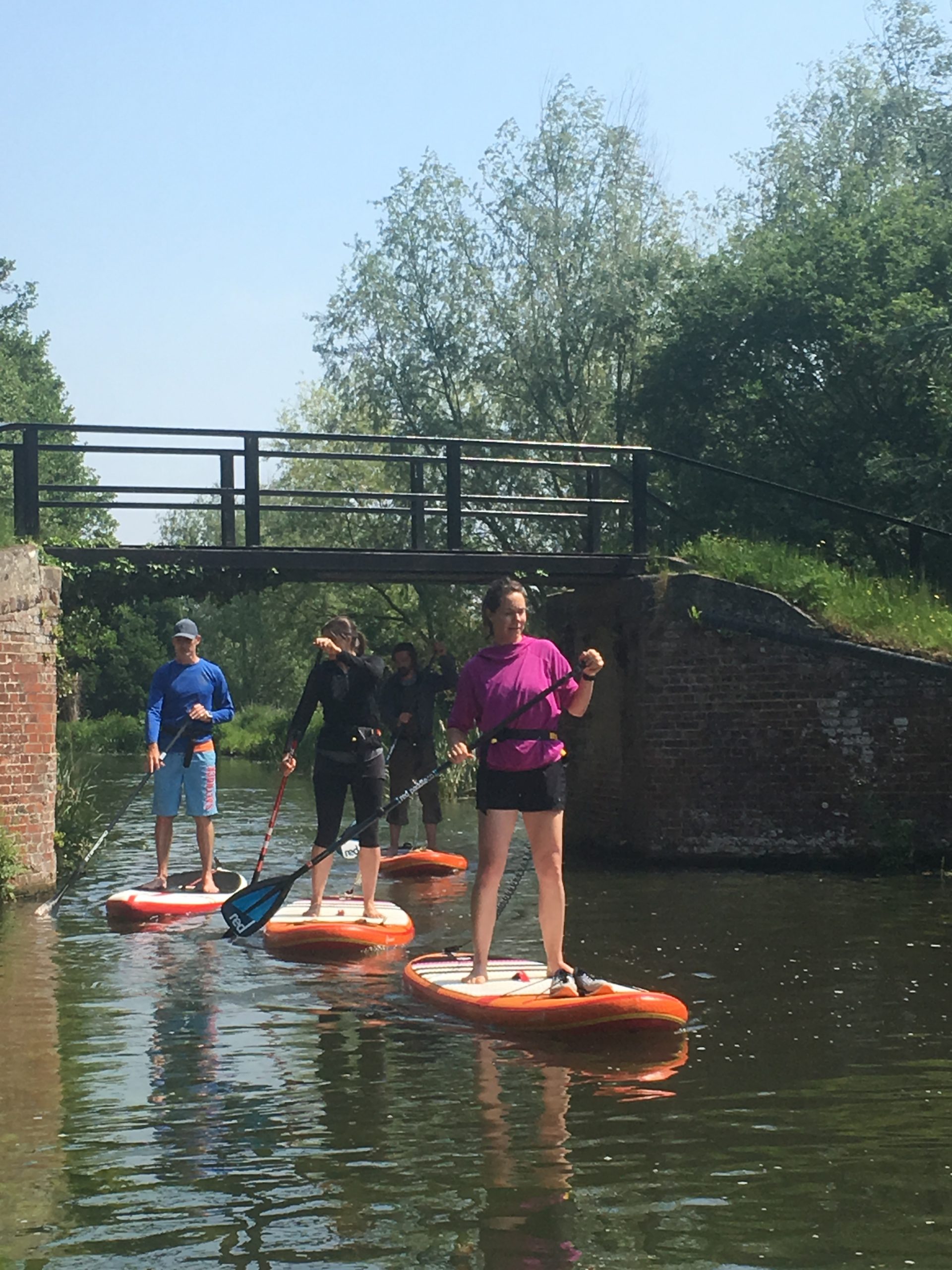 SHAC River Wey SUP safari four adults paddle boarding under footbridge